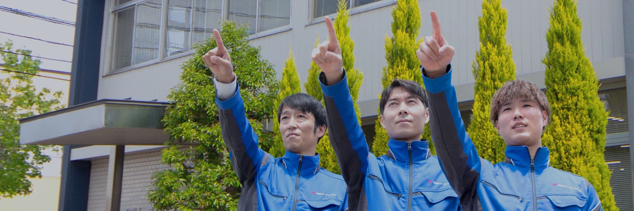 3名のスタッフが右手を上げて空に指を指している写真